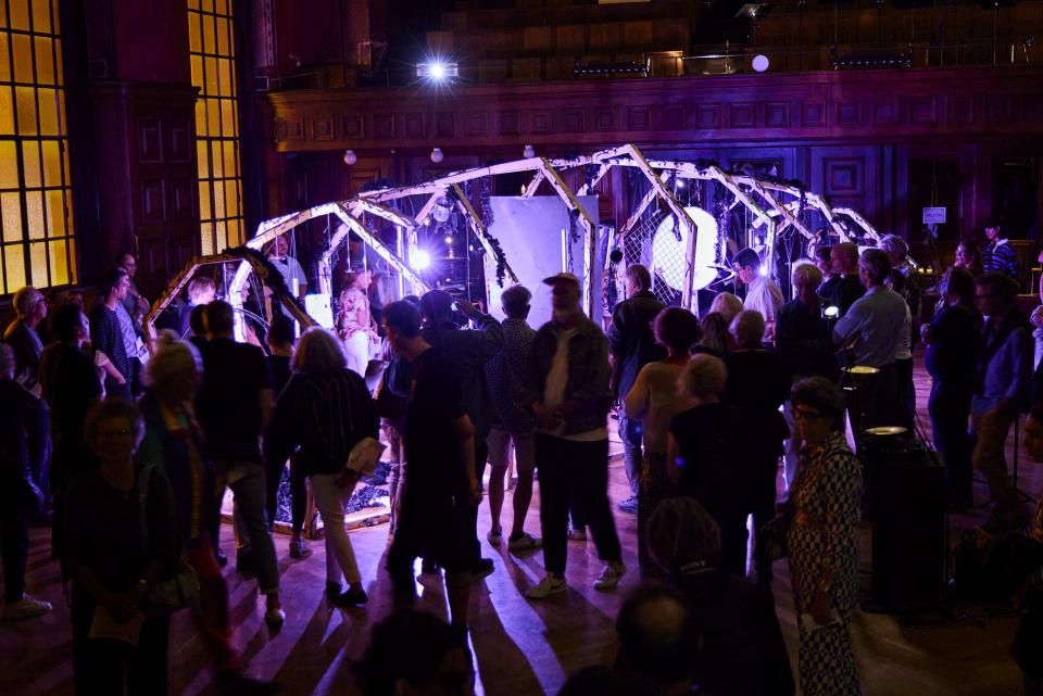 a big wooden construct reminding of a whale sceleton, in which percussion instruments hang, the structure is seen from afar with the audience surrounding it